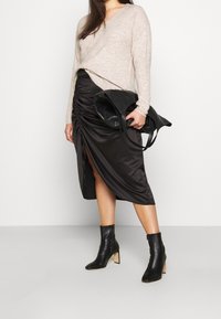 Beige gebreide trui, zwarte satijnen rok met gathered detail, en zwarte enkellaarsjes met een tan blokhak. Draagt een zwarte handtas.