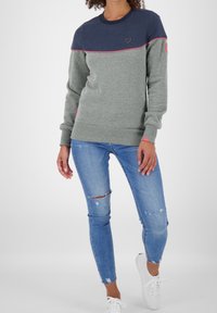 Gray and navy sweatshirt with a round neck, pink trim, and heart logo on chest, paired with distressed blue jeans and white sneakers.