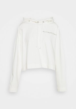 Skuren vit hoodie tillverkad av mjukt tyg med dragsko i huvan. Den har broderad text framtill och långa ärmar.