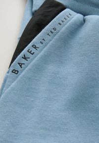 Jasnoniebieska tkanina o gładkiej fakturze z czarnym akcentem. Na metce znajduje się napis "BAKER by TED BAKER" w pogrubionej czarnej czcionce.