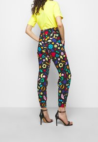 Wysokowalne, kolorowe spodnie w wzory na czarnym tle z różnymi kształtami i symbolami. Elastyczny pas i zwężane nogawki.
