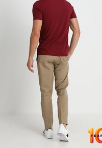 Rød kortærmet skjorte, beige slim-fit bukser og hvide sneakers med sorte detaljer. Synlige søm og rene linjer i hele outfittet.