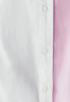 Camisa de algodón blanca con detalles en rosa, que presenta una tapeta de botones, una textura suave y colores contrastantes en el lado derecho.