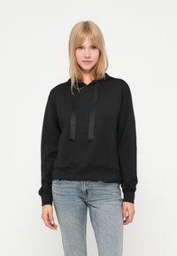 Svart bomullslue med snor, ribbet mansjetter og hem. Stoffet har en jevn tekstur, og den har en kengurulomme.