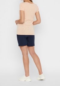 Short-sleeve light peach T-shirt paired with navy shorts and white athletic shoes, highlighting a simple, relaxed design and fit.