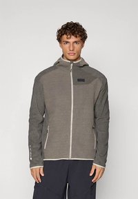 Grå teksturert glidelåssjakke med hette, kontrastglidelås og sidelommer. Har en liten logo på brystet og elastiske mansjetter.