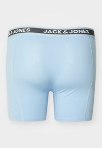 Pantaloni boxer azzurri chiari con una vita in tessuto nero che presenta la scritta "JACK & JONES." Texture liscia con dettagli di cucitura minimi.