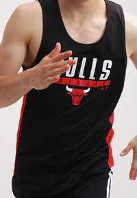 Débardeur de sport noir avec "BULLS" et logo de Chicago en rouge et blanc. Présente un design ajusté et des panneaux latéraux rouges contrastants.