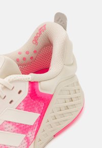 Pantofii de alergare au un superior din plasă crem, cu accente roz și o talpă texturată cu striații distincte pentru aderență. Decorat cu brandingul 'geoFIT'.