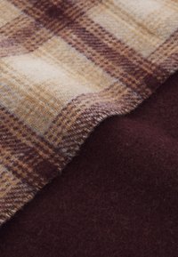 Barna és krémszínű kockás textil, amely puha tapintású, átfed egy sötét bordó egyszínű anyagot, kiemelve a kontrasztos mintákat és színeket.