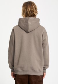 Sudadera de algodón marrón con una gran capucha ajustable, mangas largas y puños de canalé. Textura suave y corte holgado y relajado.