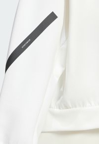 Sudadera deportiva blanca con una textura suave, que presenta una franja diagonal negra y la palabra "SPORTSWEAR" impresa en la manga.