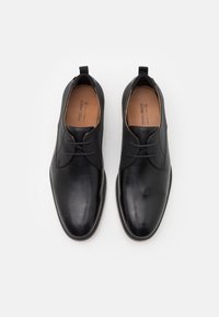 Scarpe da uomo in eco-pelle nera con finitura liscia, design con lacci, punta tonda e linguetta testurizzata. Presentano una linguetta sul retro per facilitare la calzata.