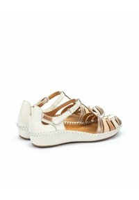 Sandales en cuir blanc avec des brides découpées et un accent beige. Présentent une semelle légèrement surélevée et cousue, ainsi qu'une étiquette sur le côté.
