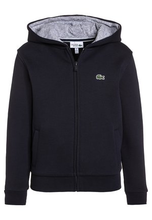 Sudadera con capucha azul marino con cremallera, forro de capucha gris, dos bolsillos frontales, puños acanalados y un pequeño logo de cocodrilo verde en el pecho.