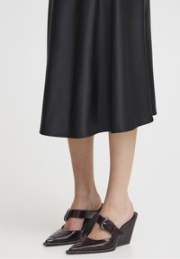 Muleit valmistatud läikivast burgundia punasest nahast, terava varbaga, laia pandlaga ja viltuse kandega. Näidatud seelik on must ja satiinsest kangast.