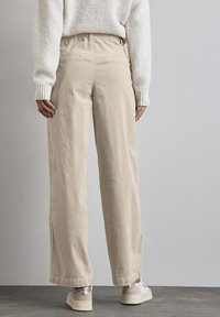 Beige corduroy wijde broek met een elastische tailleband, voorzien van zijsplitten en een textuurafwerking, gecombineerd met witte sneakers.