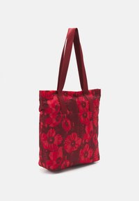 Sac fourre-tout floral rouge avec une finition brillante, présentant un motif de fleurs éclatant, de forme rectangulaire, et deux poignées en tissu robustes.