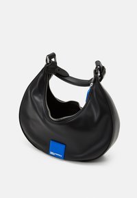 Mustavälinen nahkalaukku, jossa on kaareva muoto, hopeinen vetoketju ja sininen logopatch. Varustettu lyhyellä, säädettävällä hihnalla kantamista varten.