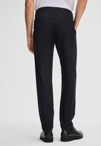 Pantaloni neri con superficie texturizzata, design a gamba dritta, passanti per cintura e due tasche posteriori. Abbinati a scarpe in pelle nere.