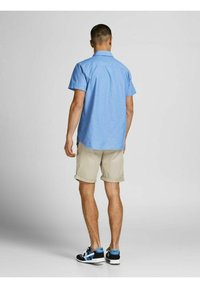 Short-sleeved, light blue shirt with a collar, paired with beige rolled shorts and black sneakers with blue accents.