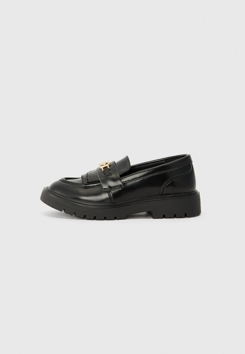 Sorte skinnloafers med en tykk gummisåle, detaljerte sømmer og en gullaccent på stroppen. Glatt tekstur og minimalistisk design.