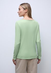 Langermige, lichtgroene top van zacht materiaal met een ontspannen pasvorm en brede halslijn, gecombineerd met lichtbeige, getextureerde brede broek.