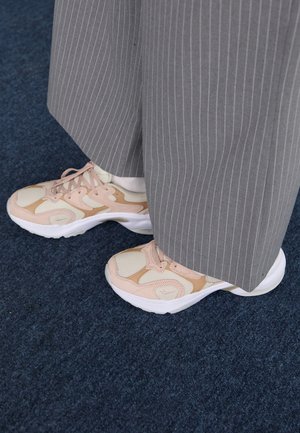 Leichte Freizeitschuhe in Creme, Rosa und Beige, mit Netzpaneelen, dicken weißen Sohlen und Schnürsenkeln, kombiniert mit grauen Nadelstreifenhosen.