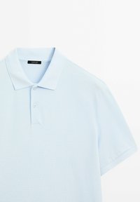Light blue polo shirt made of textured fabric, featuring a classic collar and two-button placket; label visible inside collar.