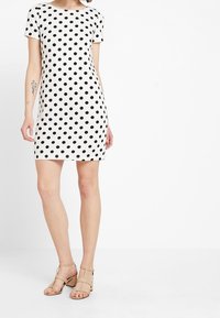 Šaty s krátkým rukávem s černobílým puntíkovaným vzorem, vyrobené z hladké tkaniny s rovnou siluetou a kulatým výstřihem.