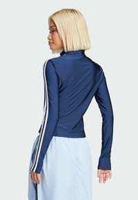 Mörkblå långärmad topp i ett slätt, elastiskt material; har vita vertikala ränder på ärmarna och en hög krage.