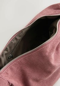Cord-Rippentasche in staubigem Rosenrot mit Reißverschluss; das Innere hat ein dunkles Futter und eine kleine Reißverschlusstasche auf einer Seite.