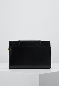 Černá kožená kabelka se strukturovaným designem, s přední klopou a embosovanou texturou. Zlaté kovové detaily a zipové uzavření.