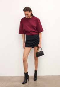 Camiseta oversize burdeos, falda ajustada negra con detalle drapeado, botines negros con punteras afiladas y un pequeño bolso negro.