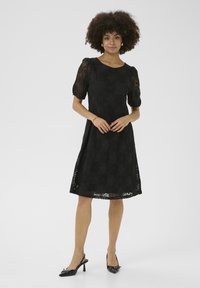 Abito in pizzo nero con maniche a palloncino corte, motivo floreale e silhouette a A. Tessuto strutturato con scollatura a girocollo e orlo a ginocchio.