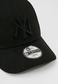 Fekete baseballsapka kiemelkedő hímzett "NY" logóval, ívelt napellenzővel, állítható pánttal és ezüst logós matricával a karimán.