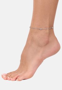 Pulsera de tobillo de plata con acentos en forma de corazón, que presenta un diseño de cadena delicado. El pie tiene un tono de piel natural y esmalte de uñas de color rosa claro.