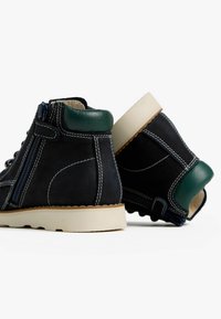 Scarpe high-top in suede nero con dettagli verdi, suola bianca e cuciture in contrasto. Presentano una cerniera laterale per una facile calzata.