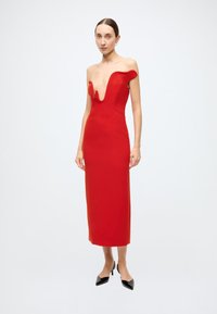 Red, sleeveless dress with a deep V-neckline and wavy edge design, fitted silhouette, knee-length, paired with black high heels.