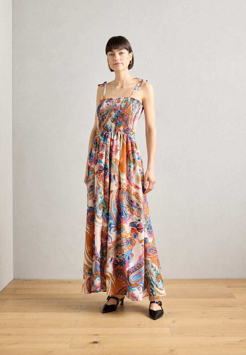 Robe maxi fabriquée en tissu léger et à motifs de couleurs rose, orange et bleu ; elle présente un corsage ajusté et des fines bretelles avec des nœuds.