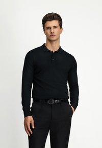 Schwarzes Langarm-Polohemd mit Kragen, ausgestattet mit drei Knöpfen. Kombiniert mit schwarzen Hosen und einem glänzenden schwarzen Gürtel. Glatte Textur.