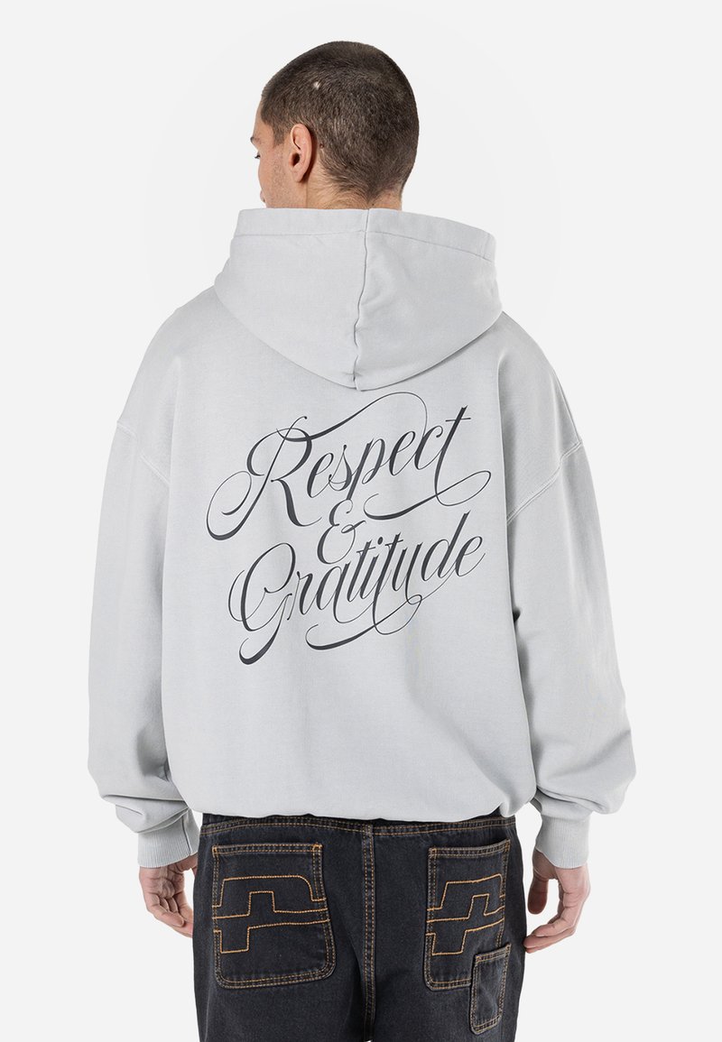 Moletom cinza claro com uma grande impressão em cursivo preto nas costas que diz "Respeito e Gratidão". Design folgado, mangas longas.