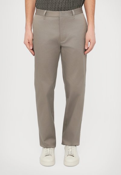 Pantaloni grigio chiaro realizzati in un tessuto liscio, con pence, passanti per cintura e tasche laterali, abbinati a sneakers bianche.
