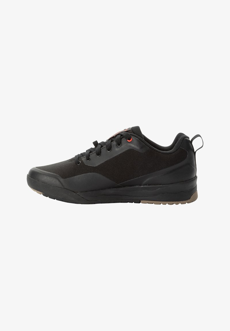 Scarpa sportiva nera con una tomaia liscia in materiale sintetico, dettagli in tessuto testurizzato, suola in gomma, design con lacci e un accento rosso vicino ai passanti.