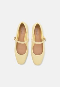 Zapatos de cuero vegano amarillos con punta redondeada, correa con hebilla lateral y un acabado suave, diseñados para un ajuste seguro.
