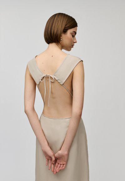 Beige jurk met een lage rug, brede banden en een strikdetail bij de hals. Gladde textuur en een aansluitende silhouet.