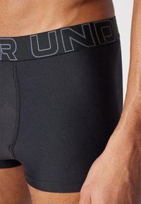 Zwarte boxershort met een gladde textuur, voorzien van een brede tailleband met contrasterend merklogo. Close-up van de stof en pasvorm.