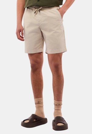 Shorts beige chiaro con vita elastica e cordoncino, dotati di tasche laterali. Indossati con sandali marroni e calze beige.