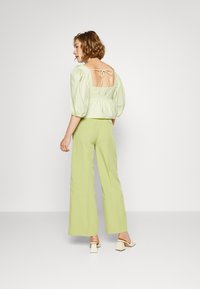 Blusa corta verde-claro com mangas bufantes e costas descobertas, combinada com calças largas de cintura alta em tom igual, acompanhada de sandálias de salto bloco.