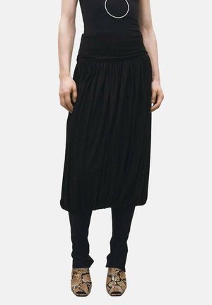 Gonna nera drappeggiata con un elastico in vita, caratterizzata da un design arricciato. Indossata con leggings neri e scarpe con tacco a fantasia.